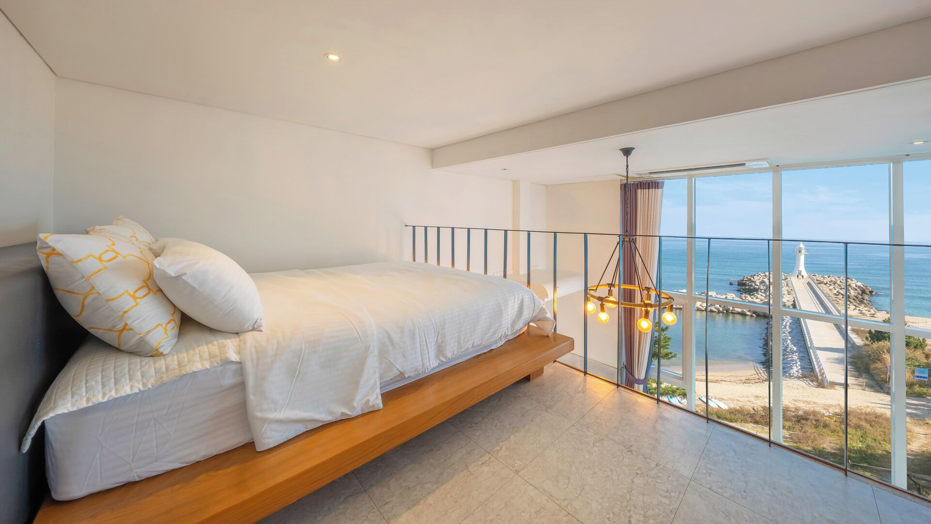 Een slaapkamer met een groot bed, uitzicht op zee en een balkon met een hekwerk.