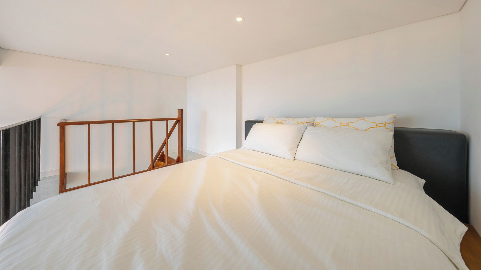 Una camera da letto con un letto grande, una scala in legno e una parete bianca e spoglia.