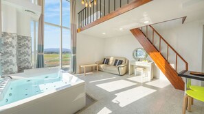 A modern room with a large window, a wooden staircase, a sofa, a desk, and a bathtub. - Gangneung Meerbrick Spa Pension (Gangneung)