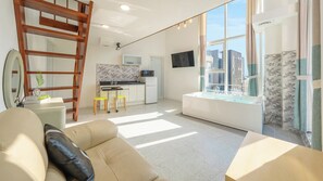 Un soggiorno moderno con un divano, una scala in legno, un angolo cottura con forno a microonde e un'ampia finestra vista edifici.