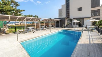 Relax by the pool surrounded by a deck and a covered seating area with tables and chairs.