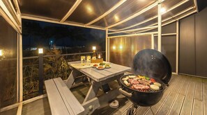 En udendørs terrasse med grill, et bord med mad og udsigt til nattehimlen.