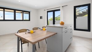 A modern kitchen with a wooden table, two chairs, and a built-in island with a sink and drawers. - Modern NEW 2BR1BA ~ Nature Escape ~ Great Location (Paradera)