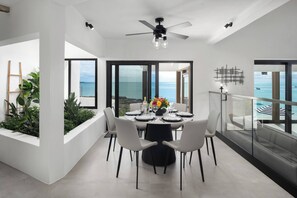 A modern dining area with a view of the ocean, a ceiling fan, and a dining table set for four.