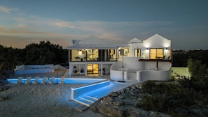 Una casa moderna de dos pisos con piscina, mobiliario exterior y vistas a la montaña.