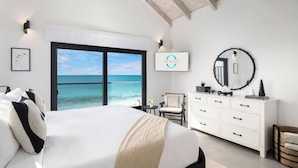 Un dormitorio con una cama, un aparador, una silla, un espejo redondo y vista al océano.