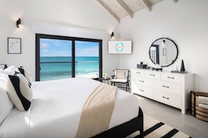 Une chambre à coucher avec un lit, une commode, une chaise, un miroir rond et une vue sur l’océan.
