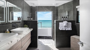 Un baño moderno con dos lavamanos, una ducha y vista al océano.