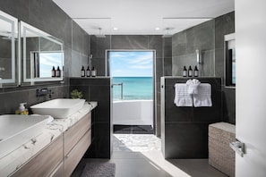 Une salle de bain moderne avec deux lavabos, une douche et une vue sur l’océan.