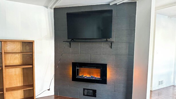 A modern living room with a fireplace, a mounted television, and a wooden shelving unit.