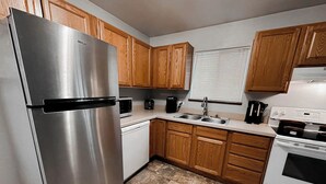 A kitchen with wooden cabinets, a stainless steel refrigerator, a white stove, and a sink.