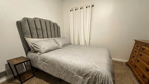 A bedroom with a bed, a nightstand, a dresser, and a window with curtains.
