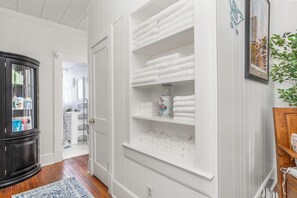 Un couloir avec une porte blanche donnant sur une salle de bain, un meuble noir avec des portes en verre et une étagère à serviettes blanche.