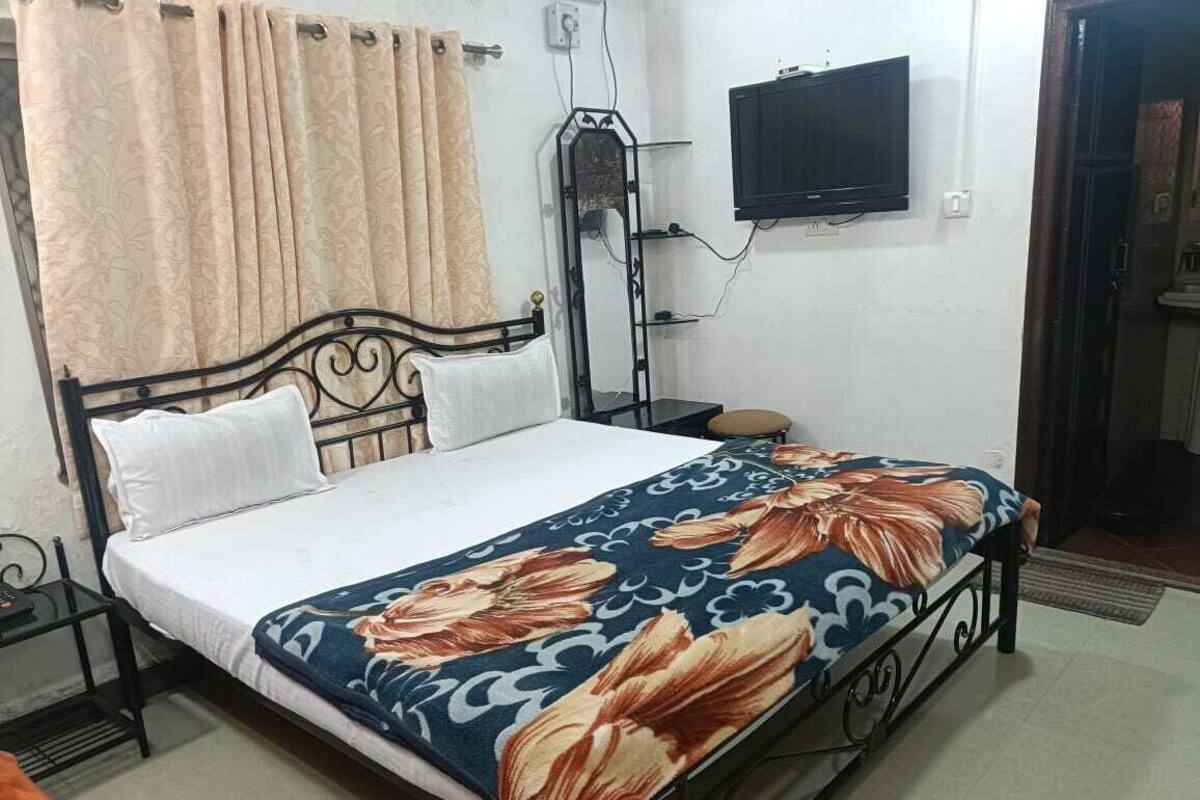 A bedroom with a bed, curtains, a TV, and a bedside table.