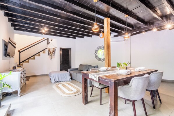 Un salon moderne avec un coin repas, comprenant un escalier, un canapé, une table basse et une table à manger en bois avec des chaises.