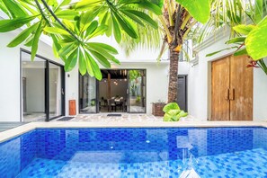 Ein moderner Poolbereich mit einem blauen, mit Fliesen ausgekleideten Pool, umgeben von üppiger Vegetation und einer Holztür.