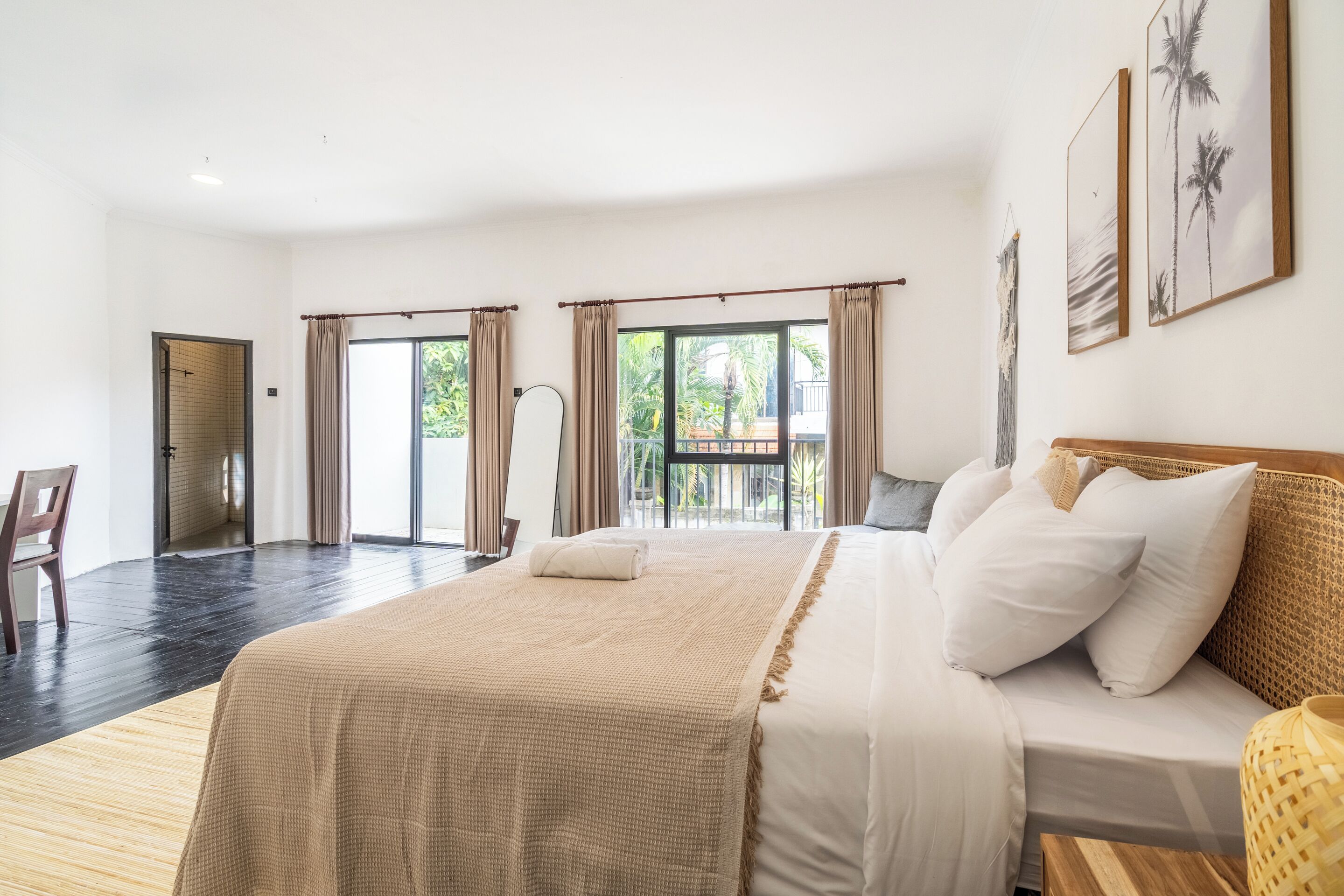 Ein geräumiges Schlafzimmer mit einem großen Bett, Holzboden, einem Balkon mit Vorhängen und Blick ins Grüne.