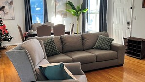 A modern living room with a grey sectional sofa, a small table, and a potted plant. - Ocean View Beach House. Sleeps 8 Coastal Luxe. Seabreeze! (Norfolk)