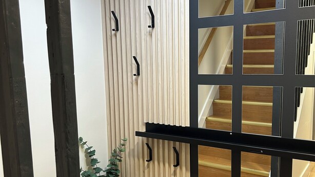 Een modern interieur met een houten paneelwand, een zwart metalen hekwerk en een trap.