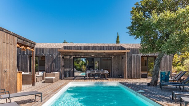 A wooden deck with a swimming pool, outdoor furniture, and a covered seating area.