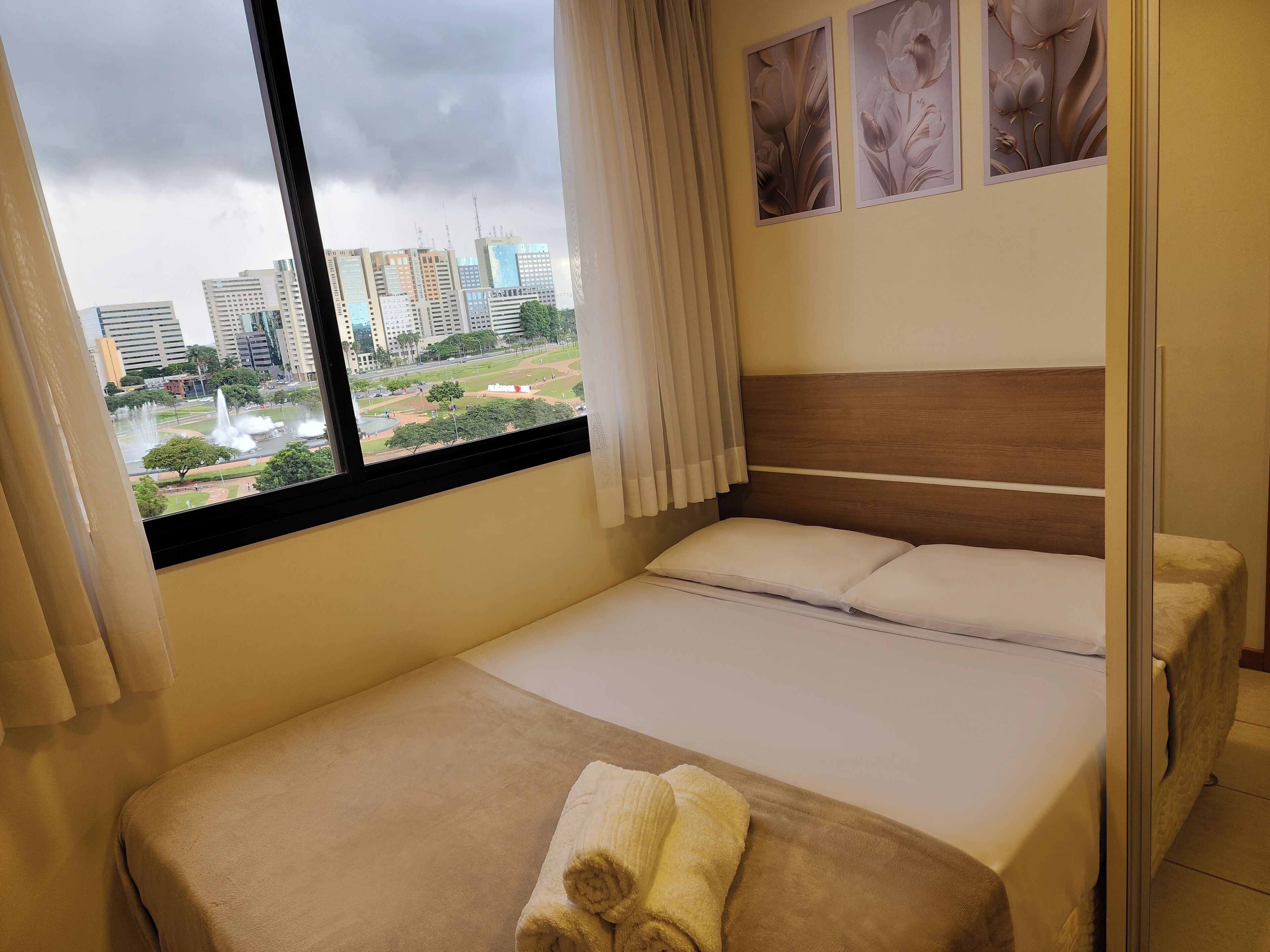 A hotel room with a bed, a window with a view of a cityscape, and a curtain.