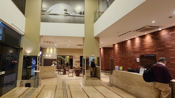 Een hotel lobby met een receptiebalie, een zithoek en een uitzicht op een gebouw door de glazen wand.