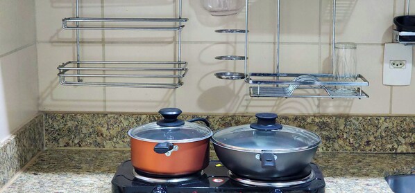Two electric kettles on a countertop with a granite backsplash, a wall-mounted shelf with glassware, and a power outlet. - ZENVA (Brasília)