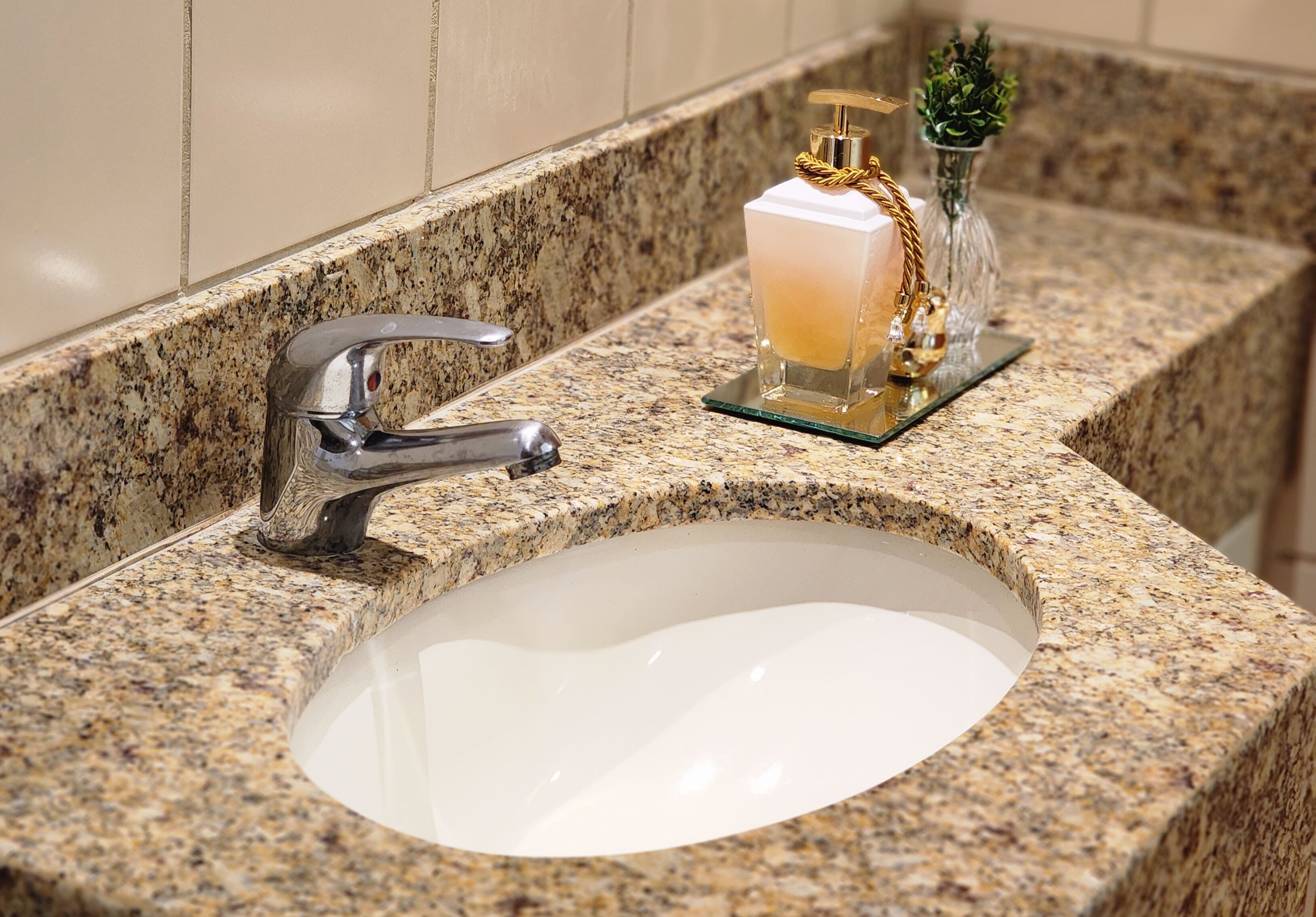 Ein Badezimmerwaschbecken mit einer Granit-Arbeitsplatte, einem Chrom-Wasserhahn und einer Glas-Seifenspender mit goldener Kette.