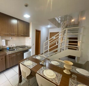 A modern kitchen with integrated appliances, a dining area with a table set for four, and an internal staircase. - ZENVA (Brasília)