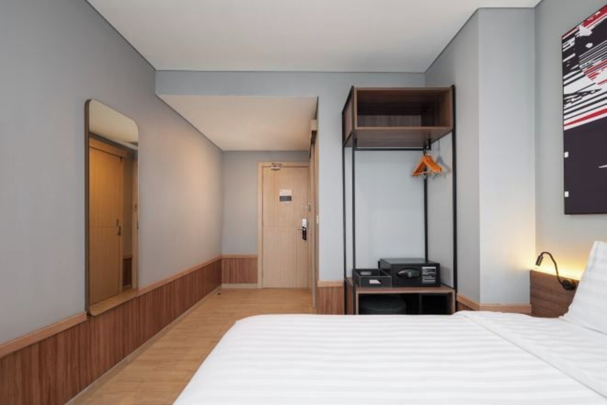 Une chambre d’hôtel comprenant un lit, une armoire, un bureau avec une lampe et un miroir.