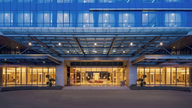 Un hotel moderno con fachada de vidrio, entrada cubierta e interior bien iluminado.