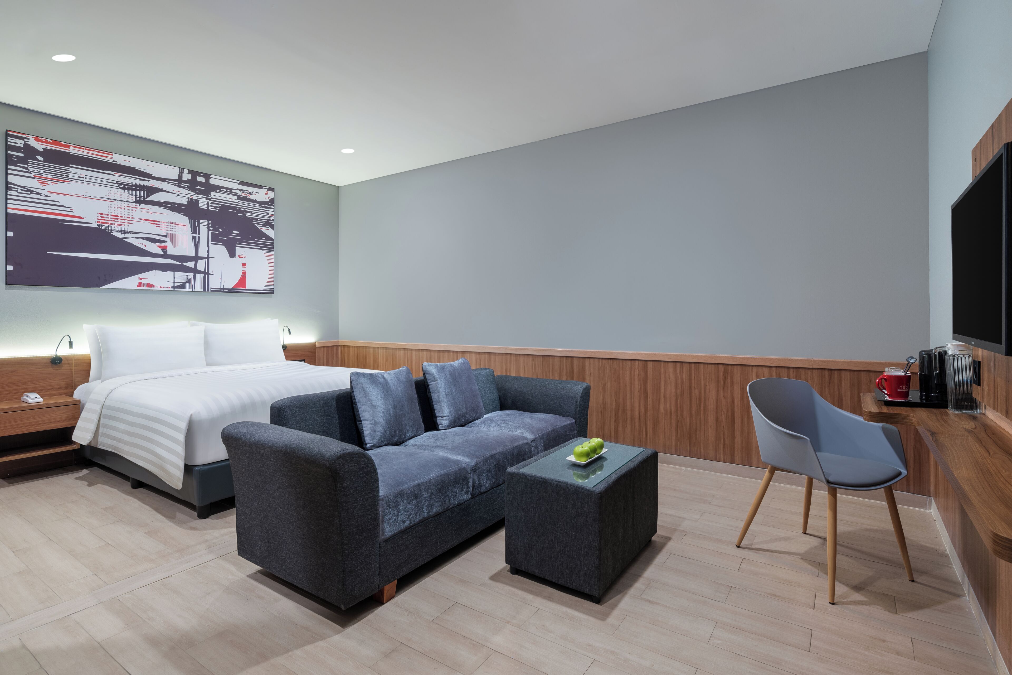 A modern hotel room with a bed, sofa, and a small table with a green object on it.