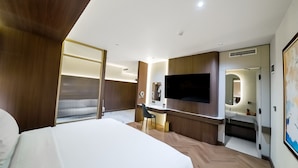 Una habitación de hotel con cama, escritorio, televisor, espejo y baño.
