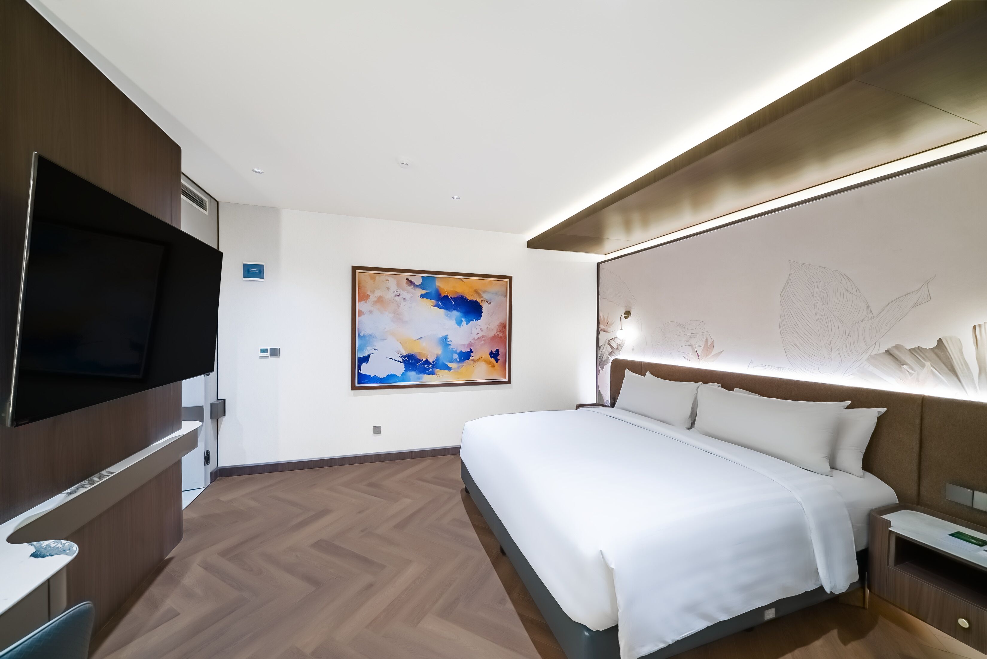 A modern hotel room with a large bed, a flat-screen TV, a painting, and a decorative headboard.
