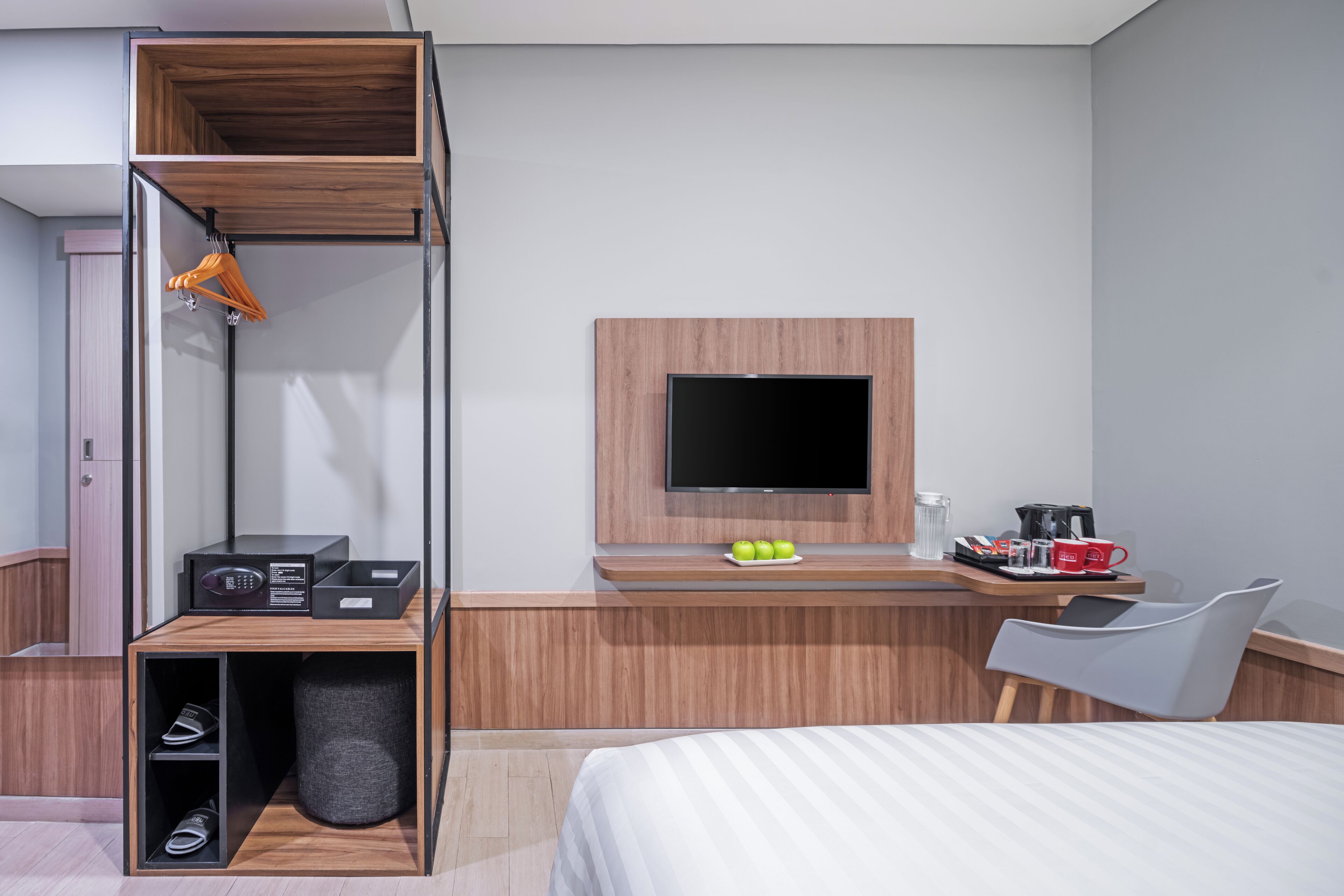Une chambre d’hôtel moderne équipée d’un lit, d’un bureau avec une télévision, d’un porte-chaussures et d’une machine à café.