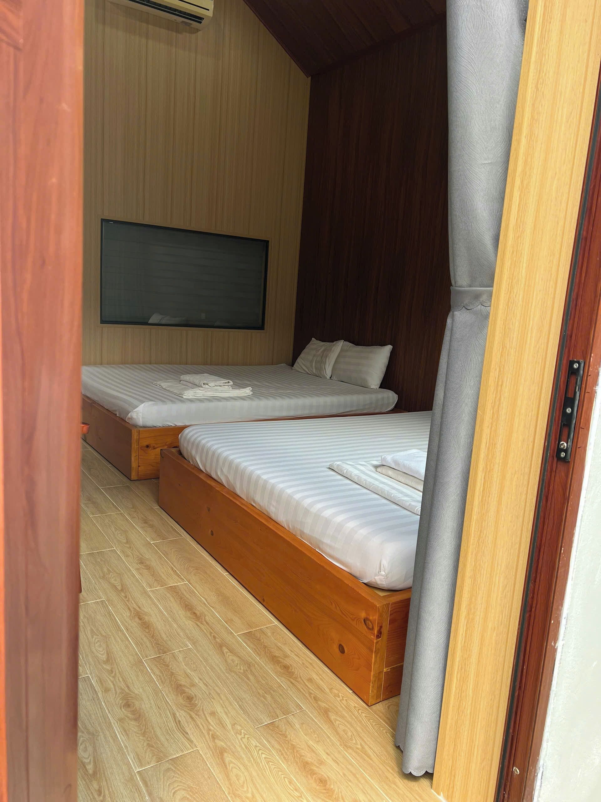 A room with two wooden beds, a mounted TV, and a wooden floor.