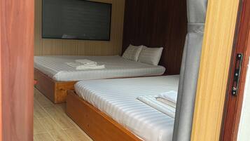 A room with two wooden beds, a mounted TV, and a wooden floor.