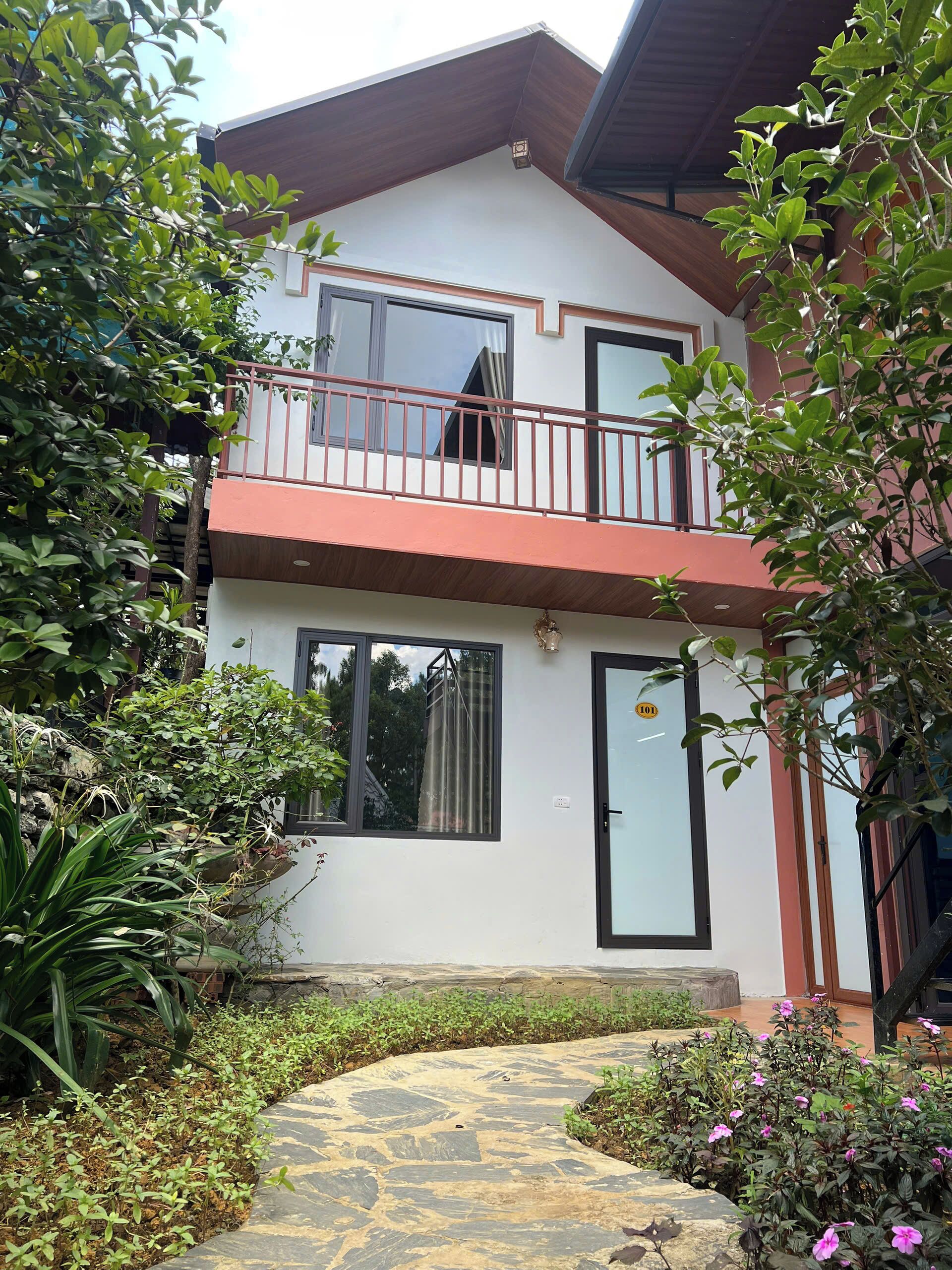 A two-story building with a balcony, a door with a number, and a stone pathway leading to the entrance.