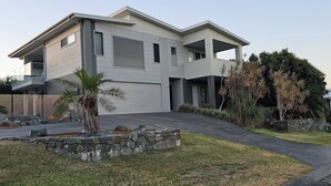 Een modern huis met twee verdiepingen, een garage, een oprit en een aangelegde voortuin met palmbomen en een stenen rand.