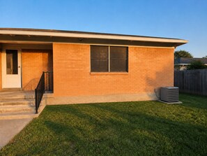 A residential house with a brick exterior, a front door, a window, a small front yard, and an air conditioning unit. - Escape to Moss Meadows: Your Serene Trip Awaits - Pet Friendly - (McKinney)