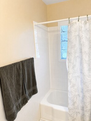 A bathroom with a bathtub, a shower curtain, and a towel rack with two towels. - Escape to Moss Meadows: Your Serene Trip Awaits - Pet Friendly - (McKinney)