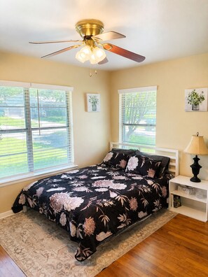 A bedroom with a bed, a ceiling fan, two windows, a nightstand, and a lamp. - Escape to Moss Meadows: Your Serene Trip Awaits - Pet Friendly - (McKinney)