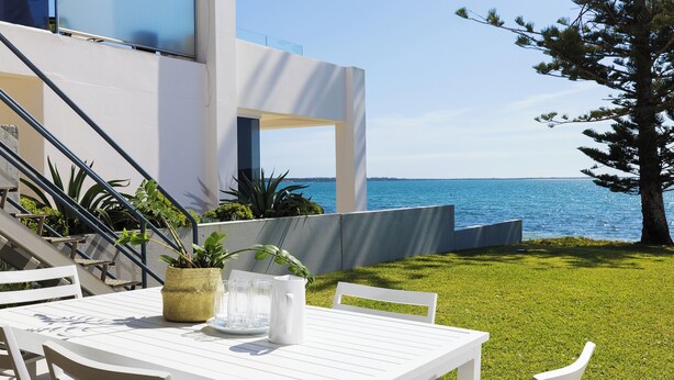 Un espace extérieur aménagé avec des sièges blancs, comprenant une table et des chaises, un pot de fleurs et une vue sur la mer.