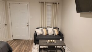 A living room with a dark grey sofa, a small coffee table with decorative items, and a white door. - Beautiful Studio Apt 5 -DnStairs (Baton Rouge)