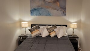 A bedroom with a bed, two bedside tables, two lamps, and a large abstract painting on the wall. - Beautiful Studio Apt 5 -DnStairs (Baton Rouge)