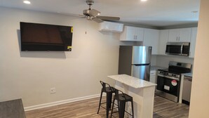 Una cocina moderna con armarios blancos, electrodomésticos de acero inoxidable, un televisor de pantalla plana y un ventilador de techo.