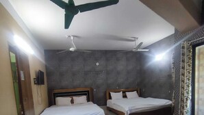 A hotel room with two single beds, a ceiling fan, a small table with a colorful cushion, and a patterned wall.