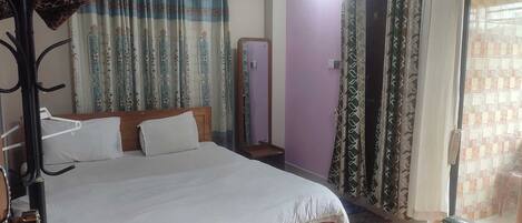 A bedroom with a bed, a small table with a remote control, and a wardrobe.