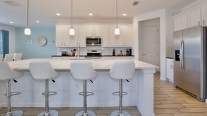 A modern kitchen with white cabinetry, a central island with bar stools, stainless steel appliances, and pendant lighting.
