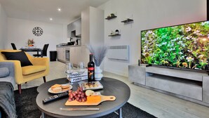A modern living room with a flat-screen TV, a dining area with a table set for two, and a kitchen in the background. - Manchester - 2-Bed Apartment - sleeps 4 - WiFi (Manchester)